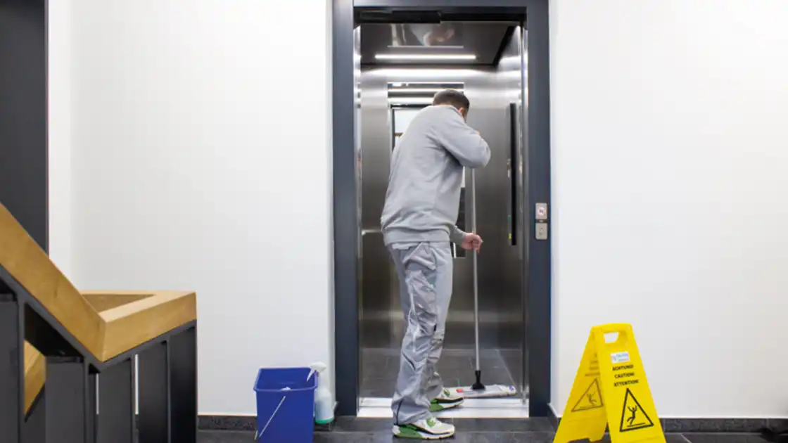 Ein Mann reinigt den Boden eines Aufzuges mit einem Bodenwischer
