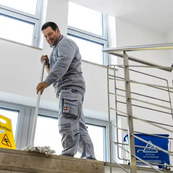 Ein Mann steht auf einem Treppenabsatz und wischt den Boden mit einem Bodenwischer