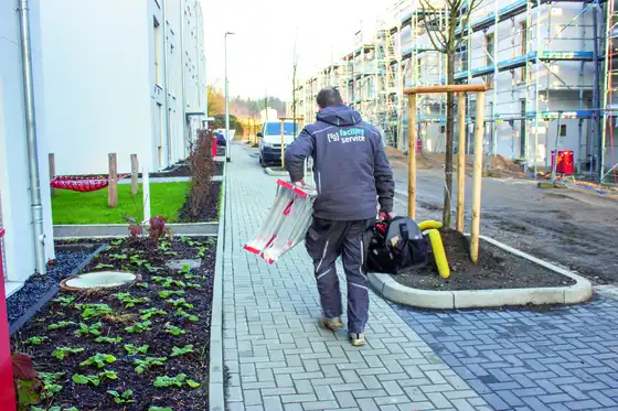 Ein Mann läuft mit Leiter und Arbeitstasche einen Weg entlang