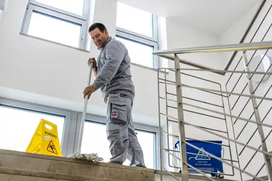 Ein Mann steht auf einem Treppenabsatz und wischt den Boden mit einem Bodenwischer